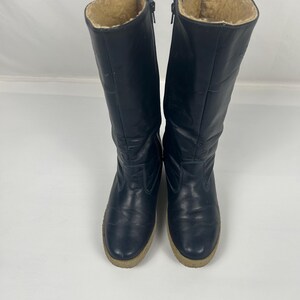 May include: A pair of navy blue knee-high boots with a beige faux fur lining. The boots have a zipper closure and a light brown sole. The boots are made of a smooth, possibly leather, material.
