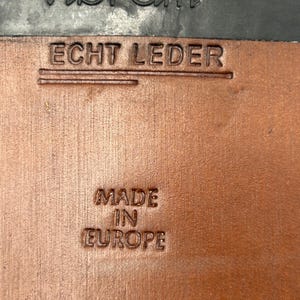 K&ouml;nnte beinhalten: Nahaufnahme einer Schuhsohle mit dem gepr&auml;gten Markennamen "Vibram" in Schwarz. Darunter sind die Worte "ECHT LEDER" in das braune Leder gestempelt. Der Text "MADE IN EUROPE" ist ebenfalls in das Leder gestempelt.