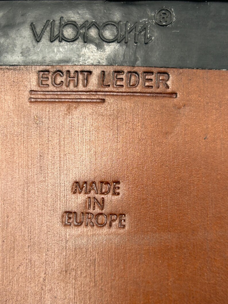 K&ouml;nnte beinhalten: Nahaufnahme einer Schuhsohle mit dem gepr&auml;gten Markennamen "Vibram" in Schwarz. Darunter sind die Worte "ECHT LEDER" in das braune Leder gestempelt. Der Text "MADE IN EUROPE" ist ebenfalls in das Leder gestempelt.