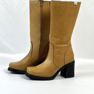 Puede incluir: Un par de botas de cuero color canela con punta cuadrada y tac&oacute;n de bloque negro. Una bota tiene una cremallera lateral. Las botas tienen suela de plataforma, sobre fondo blanco.