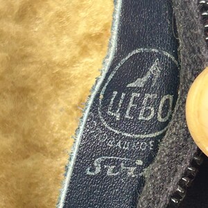 May include: Close-up of a dark blue leather boot interior with a light brown, fuzzy lining. A circular logo with Cyrillic text and a shoe graphic is visible. A black zipper is on the right side.