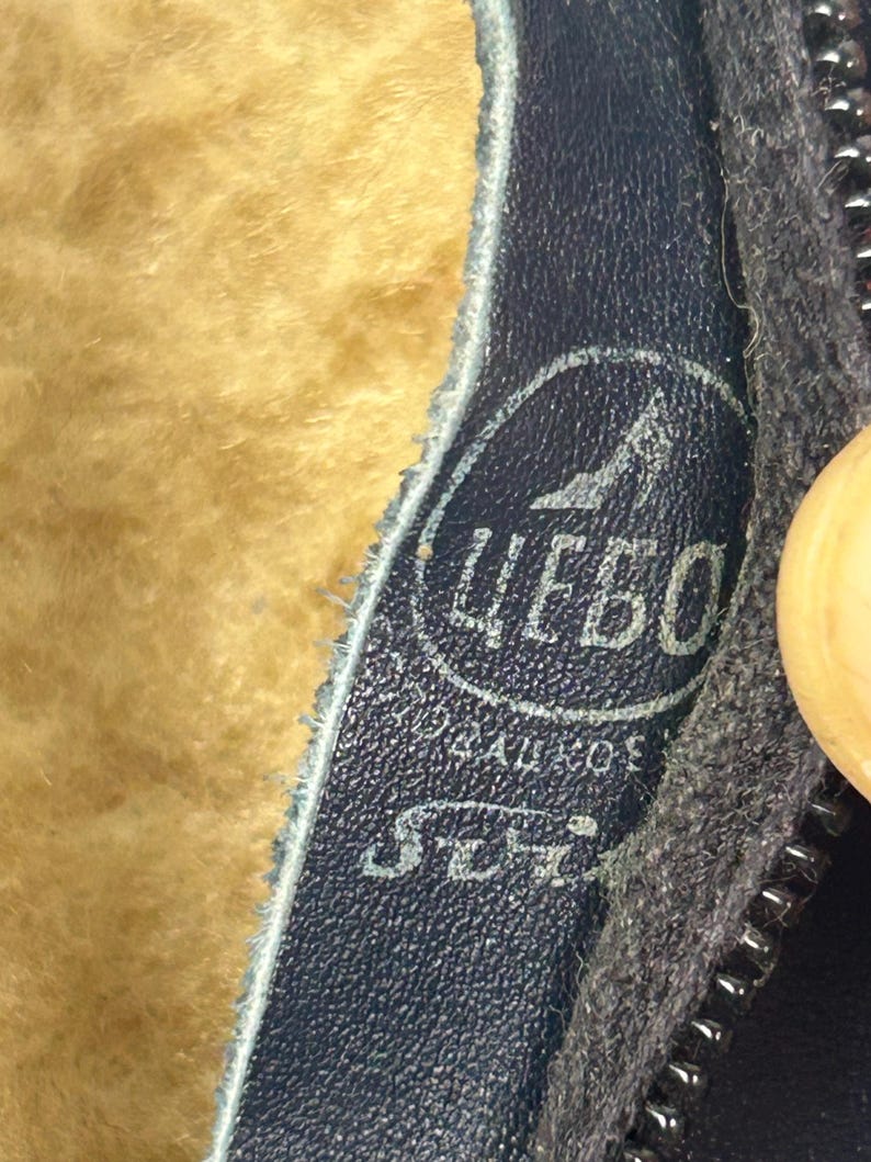 May include: Close-up of a dark blue leather boot interior with a light brown, fuzzy lining. A circular logo with Cyrillic text and a shoe graphic is visible. A black zipper is on the right side.