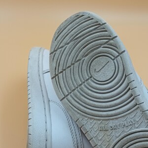 以下が含まれることがあります： 白い革のハイカットスニーカーで、白いゴム製のソールが付いています。ソールには円形の模様があり、底には「All Day Play」という文字が印刷されています。