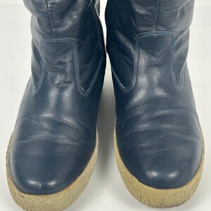 May include: A pair of navy blue, knee-high boots. The boots have a rounded toe and a thick, light brown sole. The upper portion of the boots is made of a smooth, slightly textured material.
