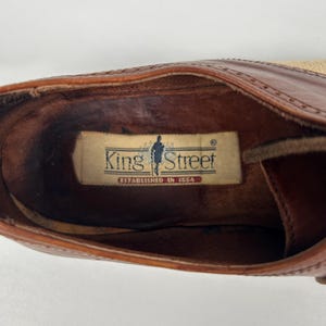 May include: Close-up of a brown leather shoe interior. The shoe features a label that reads "King Street Established in 1954". The shoe has a light tan sole and a dark brown leather upper.
