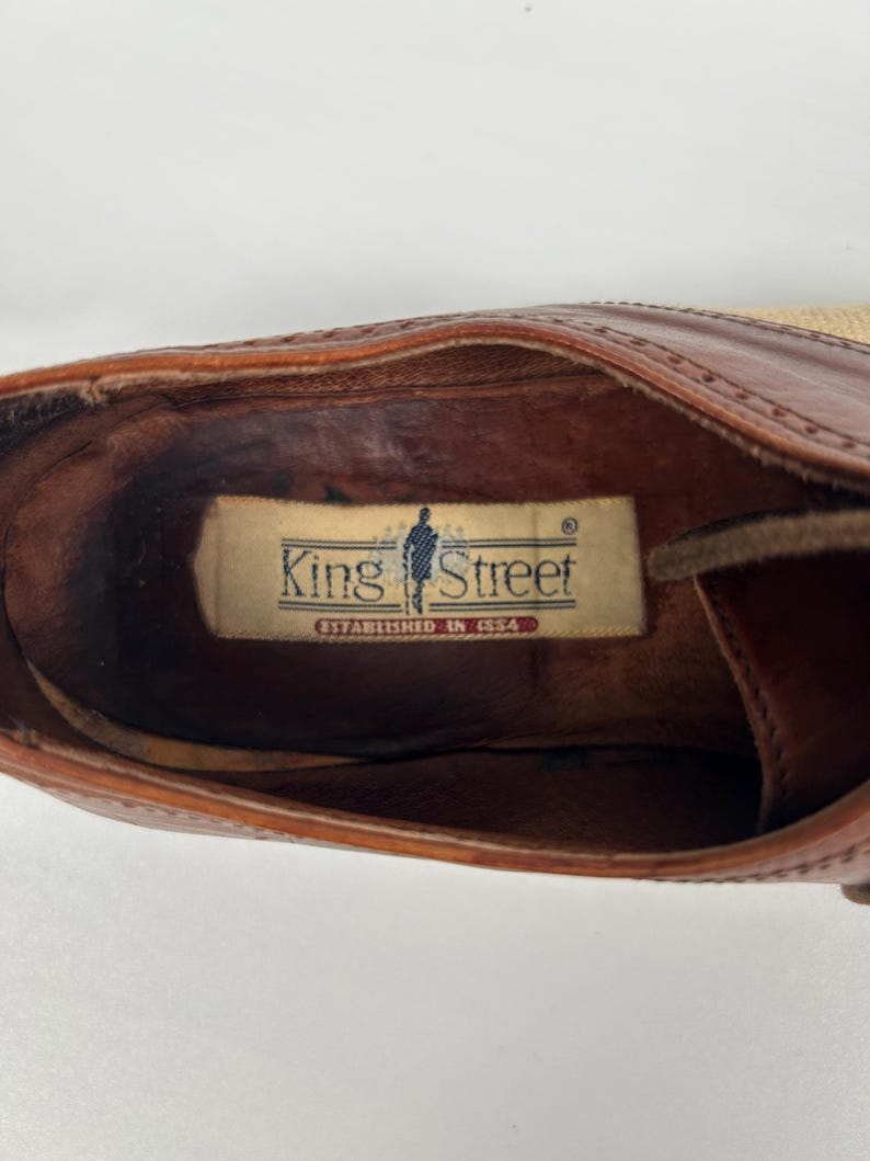 May include: Close-up of a brown leather shoe interior. The shoe features a label that reads "King Street Established in 1954". The shoe has a light tan sole and a dark brown leather upper.