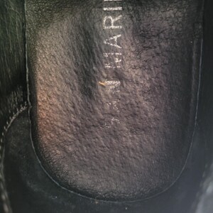 May include: Close-up of the inside of a black leather shoe with the word "Marina" printed on the insole.
