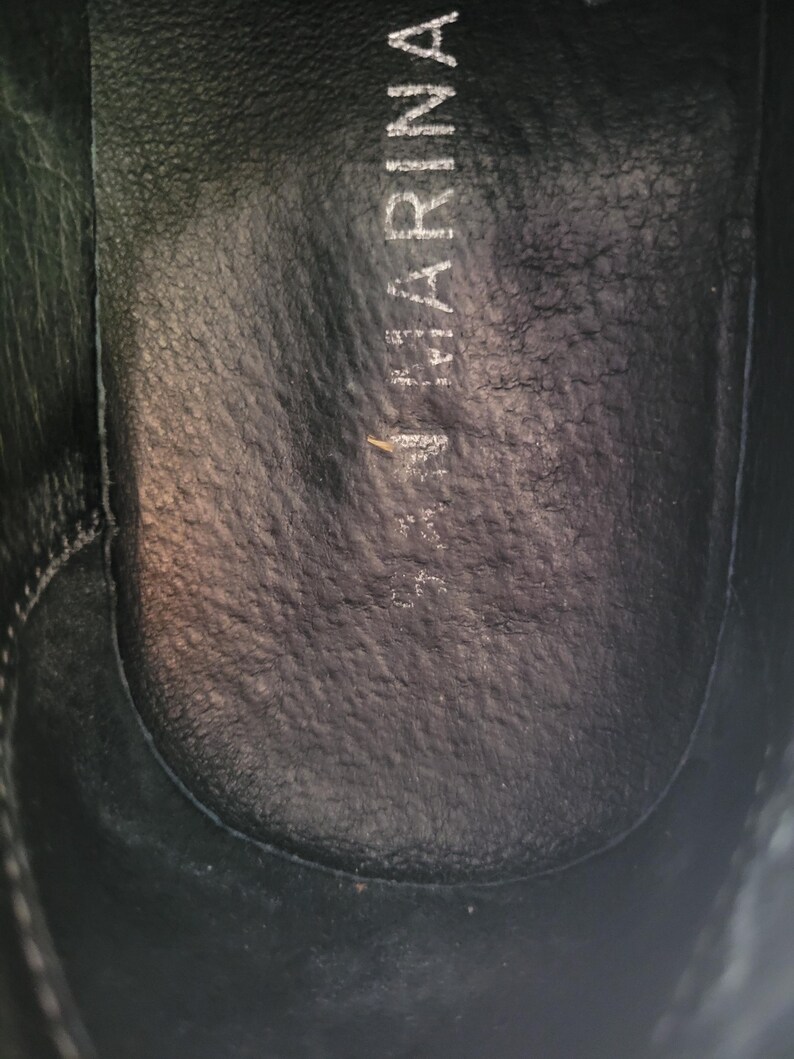 May include: Close-up of the inside of a black leather shoe with the word "Marina" printed on the insole.