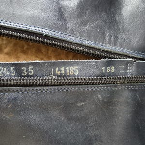May include: Close-up of a black leather boot with a partially open zipper. Visible numbers include "245 35" and "141185" on the leather. The interior lining is a light brown color. The boot appears to be well-worn.