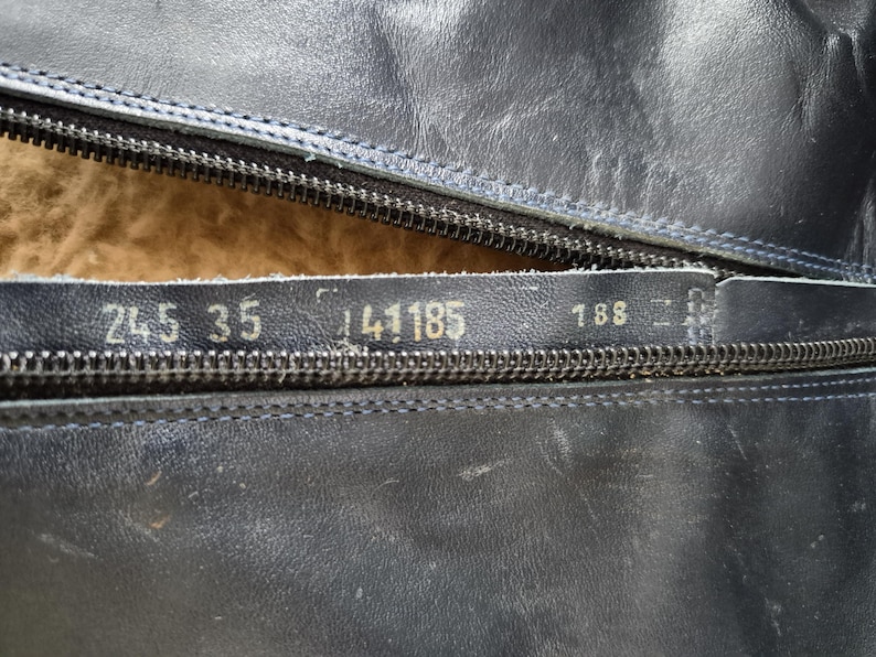 May include: Close-up of a black leather boot with a partially open zipper. Visible numbers include "245 35" and "141185" on the leather. The interior lining is a light brown color. The boot appears to be well-worn.