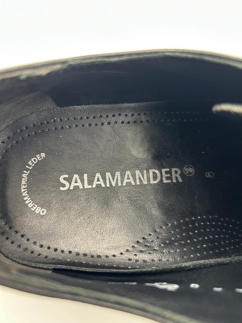 K&ouml;nnte beinhalten: Nahaufnahme des Inneren eines schwarzen Lederschuhs. Die Innensohle tr&auml;gt den Markennamen "SALAMANDER" in wei&szlig;en Buchstaben. Die Schuhgr&ouml;&szlig;e ist mit "8" angegeben. Die Worte "OBERMATERIAL LEDER" sind ebenfalls sichtbar.