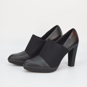 May include: A pair of black heeled shoes with a black elastic panel and the brand name "Calvin Klein" on the side.