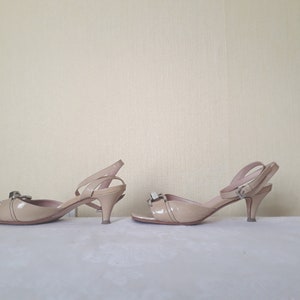 May include: A pair of beige heeled sandals with a buckle detail on the ankle strap. The sandals have a pointed toe and a thin heel.