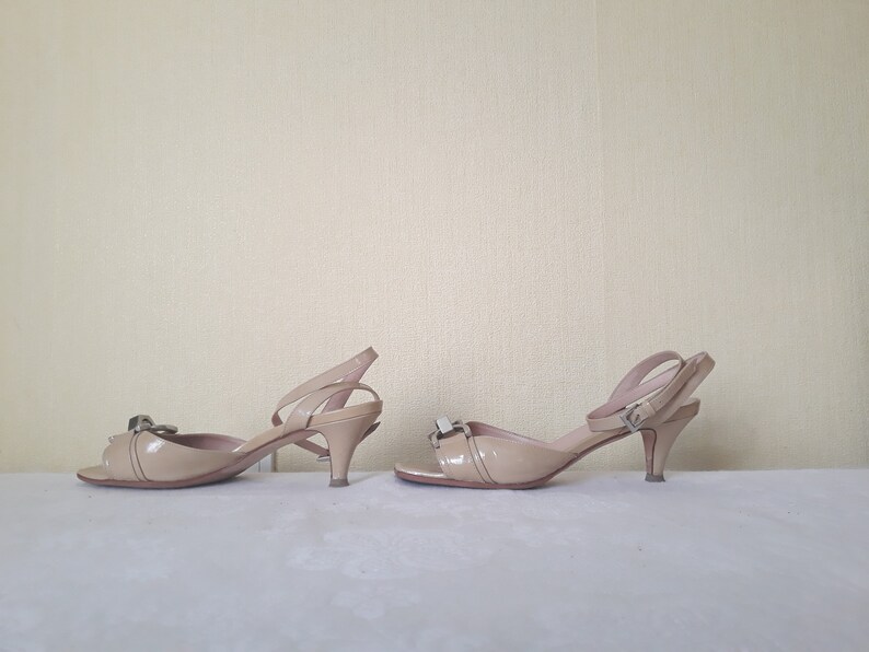May include: A pair of beige heeled sandals with a buckle detail on the ankle strap. The sandals have a pointed toe and a thin heel.