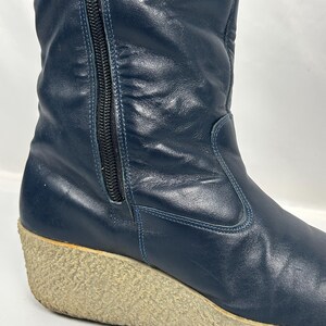 May include: Navy blue leather boot with a wedge sole. The boot features a side zipper and a textured, light-colored sole. The leather has a slight sheen, and the boot appears to be vintage.
