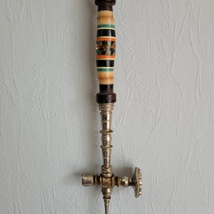 May include: A silver and wooden decorative tool with a long handle and a cross-shaped head. The handle is decorated with colorful stripes and a floral design.