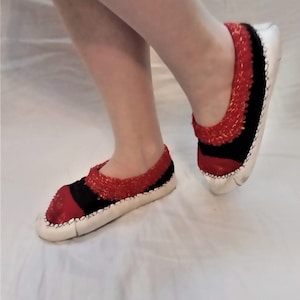Puede incluir: Un par de zapatillas de punto rojas y negras con suelas blancas. Las zapatillas están hechas de un material suave y cómodo y tienen un diseño simple y elegante.