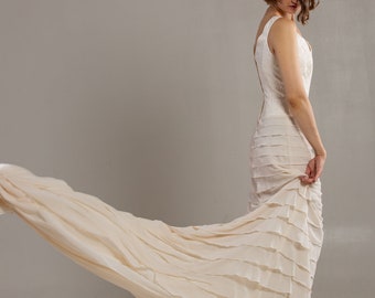 May include: A woman in a white wedding dress with a flowing skirt and a flower crown in her hair. She is standing on a light gray background.