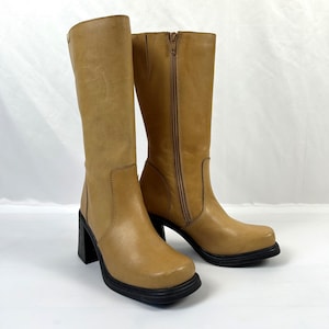 Puede incluir: Botas altas de cuero color canela con punta cuadrada y suela negra. Las botas tienen tac&oacute;n de bloque y cierre de cremallera lateral. Las botas miden aproximadamente 30 cm de altura.