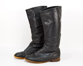 May include: A pair of black leather boots with a slouchy look. The boots have a rounded toe and a low heel.