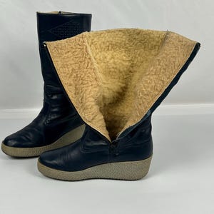 May include: A pair of navy blue winter boots with a faux fur lining. The boots have a zipper closure and a light gray sole. One boot is partially unzipped, revealing the tan interior.