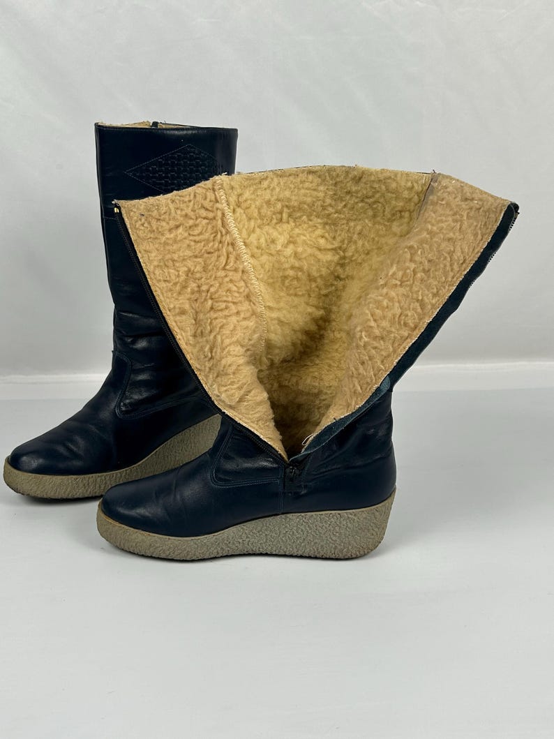 May include: A pair of navy blue winter boots with a faux fur lining. The boots have a zipper closure and a light gray sole. One boot is partially unzipped, revealing the tan interior.