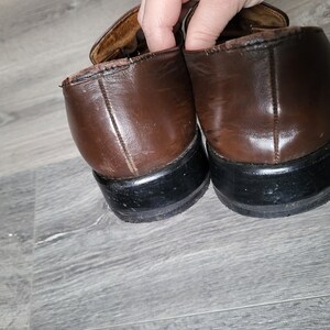 May include: A pair of brown leather shoes with black soles. The shoes have a buckle detail on the top.