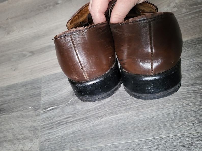 May include: A pair of brown leather shoes with black soles. The shoes have a buckle detail on the top.