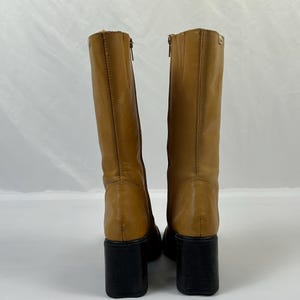 Puede incluir: Botas altas de cuero color marr&oacute;n claro con tacones de bloque negros. Las botas tienen cierre de cremallera y punta redondeada. Est&aacute;n hechas de cuero liso y tienen un ligero brillo. Los tacones miden unos 7,6 cm de alto.