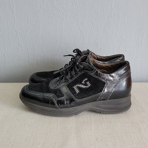 Puede incluir: Par de zapatillas negras con suela de plataforma. Los zapatos presentan una combinación de ante y charol, con un diseño decorativo de pedrería en el lateral. Los cordones son negros.