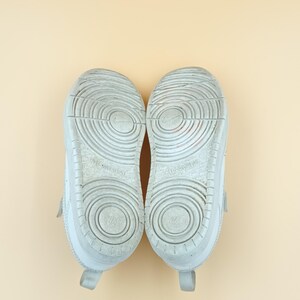 以下が含まれることがあります： テクスチャ加工されたソールが付いた白いスニーカーのペア。ソールは円形の模様で、「Non-Marking」という文字がソールに表示されています。