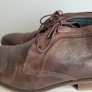 May include: A pair of brown leather ankle boots with laces. The boots have a slightly distressed look and are made of a soft, supple leather.