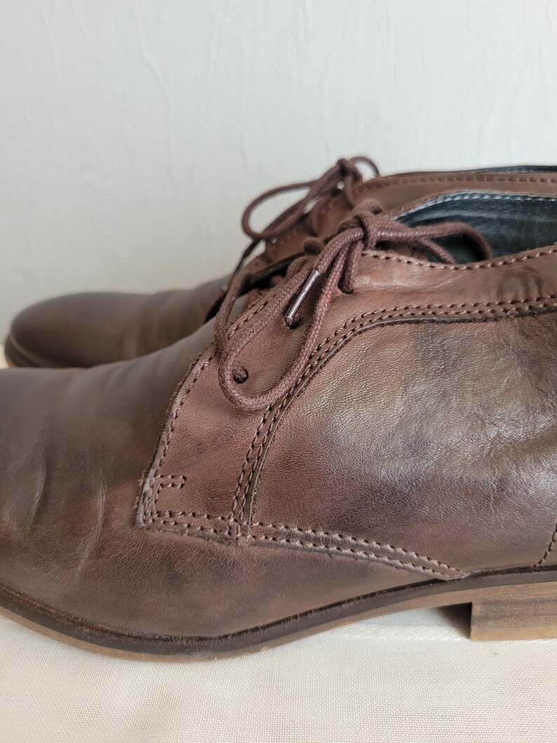 May include: A pair of brown leather ankle boots with laces. The boots have a slightly distressed look and are made of a soft, supple leather.