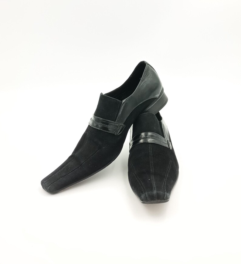 Puede incluir: Un par de zapatos de vestir de ante negro con punta puntiaguda y ribete de cuero negro. Los zapatos tienen un dise&ntilde;o sutilmente texturizado.