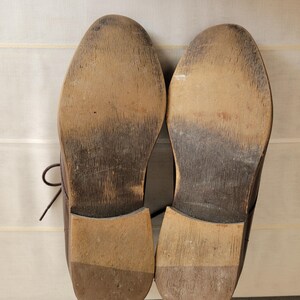 May include: A pair of brown leather shoes with worn soles. The shoes have a lace-up design and are made of a smooth leather.