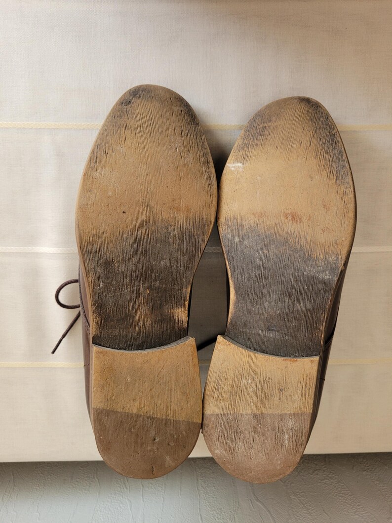 May include: A pair of brown leather shoes with worn soles. The shoes have a lace-up design and are made of a smooth leather.