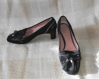 Könnte beinhalten: Ein Paar schwarze Wildleder-Loafer mit niedrigem Blockabsatz, verziert mit Fransen an der Schuhspitze, silberfarbenen Metallelementen und weißen Kontrastnähten. Das Innere der Schuhe ist mit einem hellrosa Material ausgekleidet.