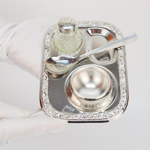 May include: A silver serving tray with a small bowl, a salt shaker, and a spoon. The tray has a decorative border.