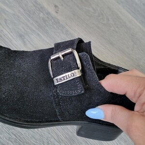 K&ouml;nnte beinhalten: Schwarzer Wildlederschuh mit einer silbernen Schnalle, auf der "ESTILO" steht.