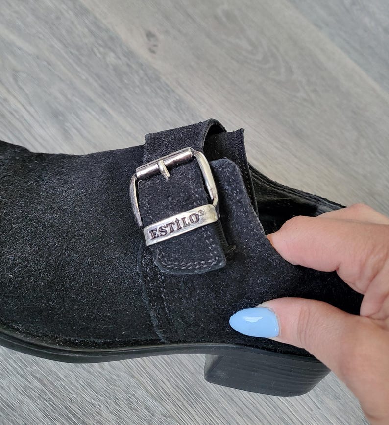 K&ouml;nnte beinhalten: Schwarzer Wildlederschuh mit einer silbernen Schnalle, auf der "ESTILO" steht.