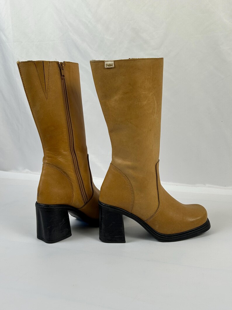 Puede incluir: Botas altas de cuero color canela con tacones de bloque negros. Una bota tiene una cremallera lateral. Las botas tienen punta cuadrada y una peque&ntilde;a etiqueta en la parte superior. Los tacones miden unos 7,6 cm.