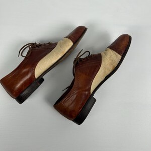 May include: A pair of two-tone oxford shoes. The shoes feature brown leather uppers with tan fabric panels on the sides and toes. The shoes have brown laces and black soles.