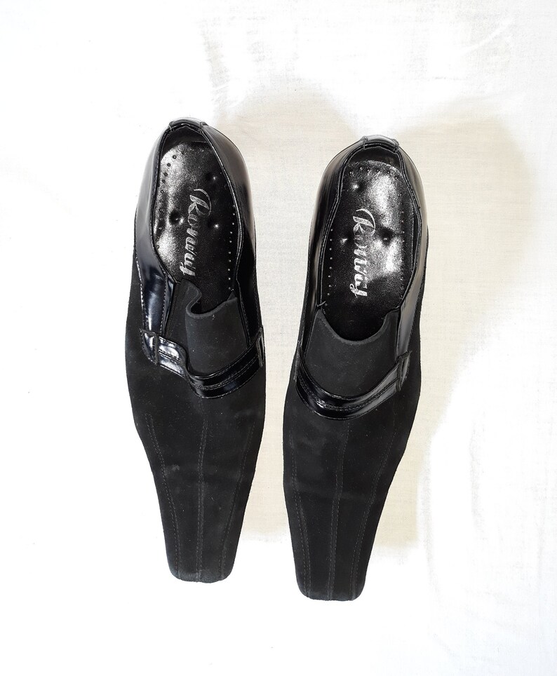 Puede incluir: Un par de zapatos de ante negro con ribete de charol negro. Los zapatos tienen punta puntiaguda y tac&oacute;n bajo. El nombre de la marca "Runway" est&aacute; impreso en el interior de cada zapato.