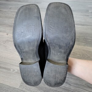 K&ouml;nnte beinhalten: Ein Paar schwarze Lederschuhe mit einer strukturierten Sohle. Die Schuhe sind abgenutzt und haben etwas Schmutz an den Sohlen.