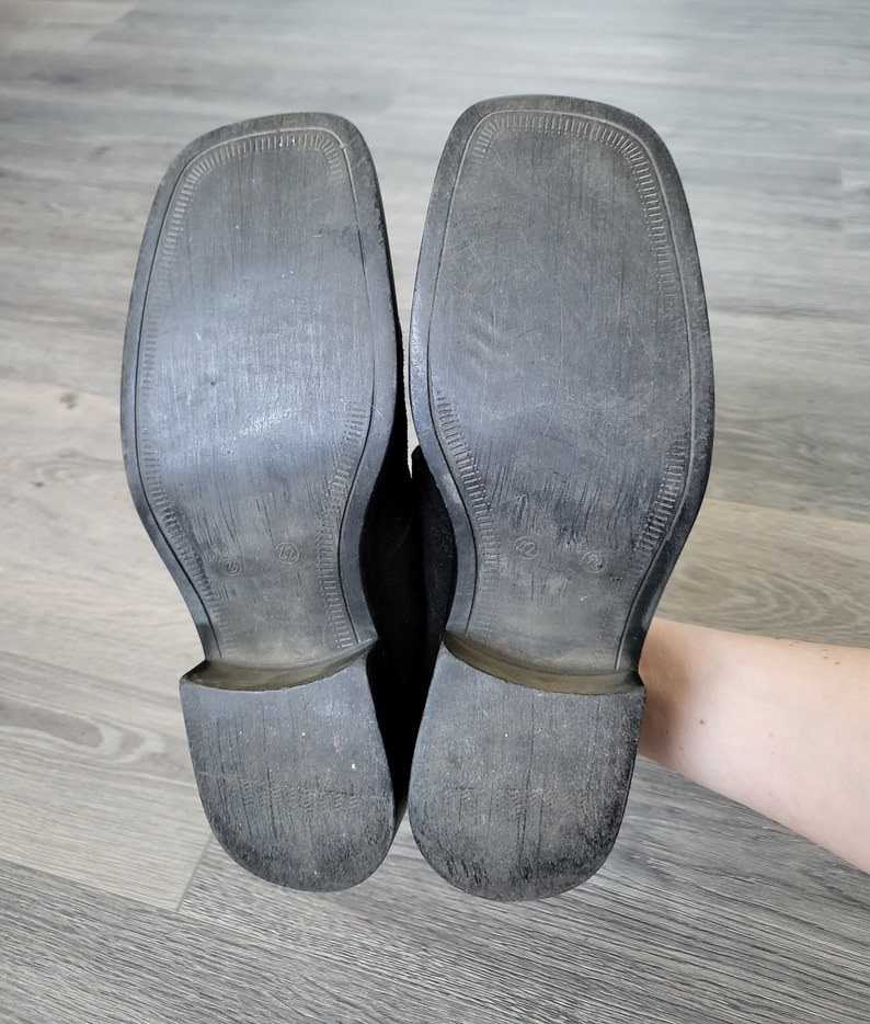 K&ouml;nnte beinhalten: Ein Paar schwarze Lederschuhe mit einer strukturierten Sohle. Die Schuhe sind abgenutzt und haben etwas Schmutz an den Sohlen.