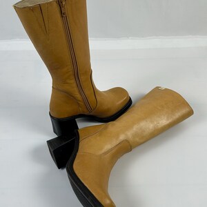 Puede incluir: Un par de botas altas de cuero color canela. Las botas tienen una cremallera lateral, una puntera redondeada y un tac&oacute;n de bloque negro. Las botas miden aproximadamente 35.5 cm de altura.