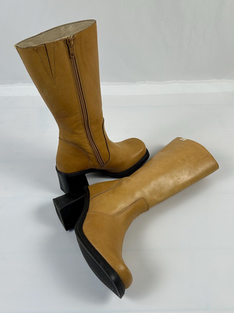 Puede incluir: Un par de botas altas de cuero color canela. Las botas tienen una cremallera lateral, una puntera redondeada y un tac&oacute;n de bloque negro. Las botas miden aproximadamente 35.5 cm de altura.