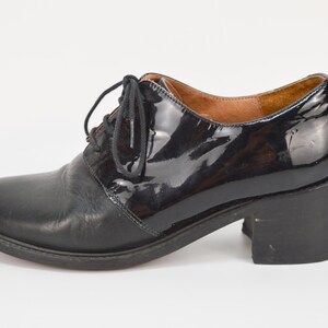 Puede incluir: Zapatos de tac&oacute;n de cuero negro con puntera de charol y cierre de cordones.