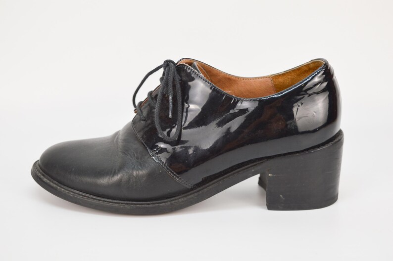 Puede incluir: Zapatos de tac&oacute;n de cuero negro con puntera de charol y cierre de cordones.