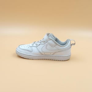 以下が含まれることがあります： ベルクロストラップとナイキのスウッシュロゴが付いた白い革製のローカットスニーカー